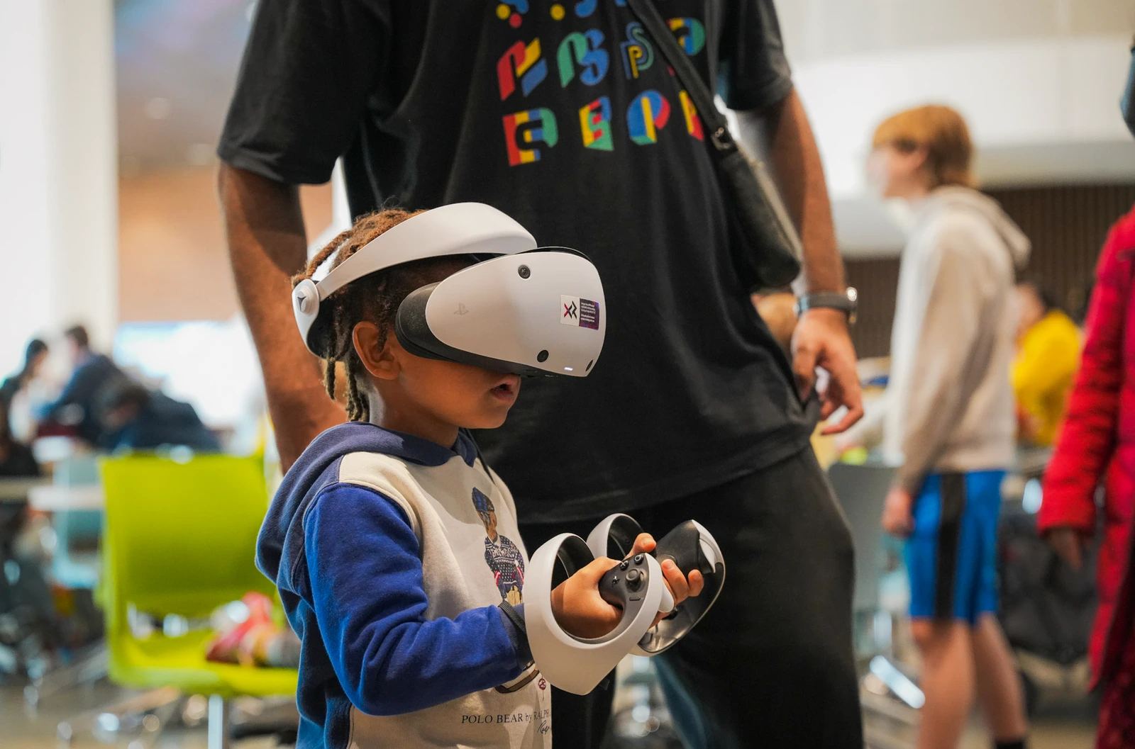 A young visitor trying a VR headset and controllers at an XR event.
